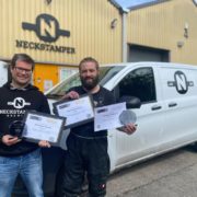 Photo of Adam the Owner of Neckstamper and Jo the head brewer in front of their branded van, holding certificates they have won for their beers. Here Adam is interviewed for #BeerTogether