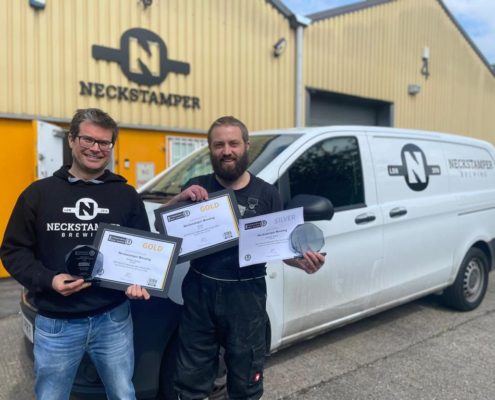 Photo of Adam the Owner of Neckstamper and Jo the head brewer in front of their branded van, holding certificates they have won for their beers. Here Adam is interviewed for #BeerTogether